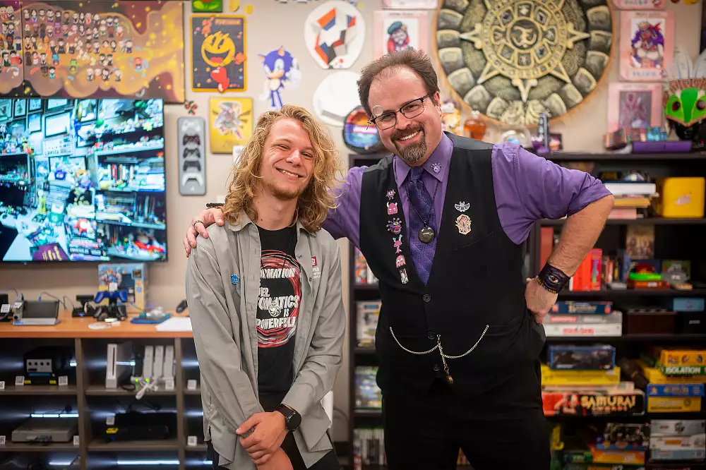 A front view of MARLA Council members Haven Hamelin on the left and Mathew Powers on the right with their hands over each others' shoulders smiling in the lab against many different posters, prints, and memorbilia in the lab.